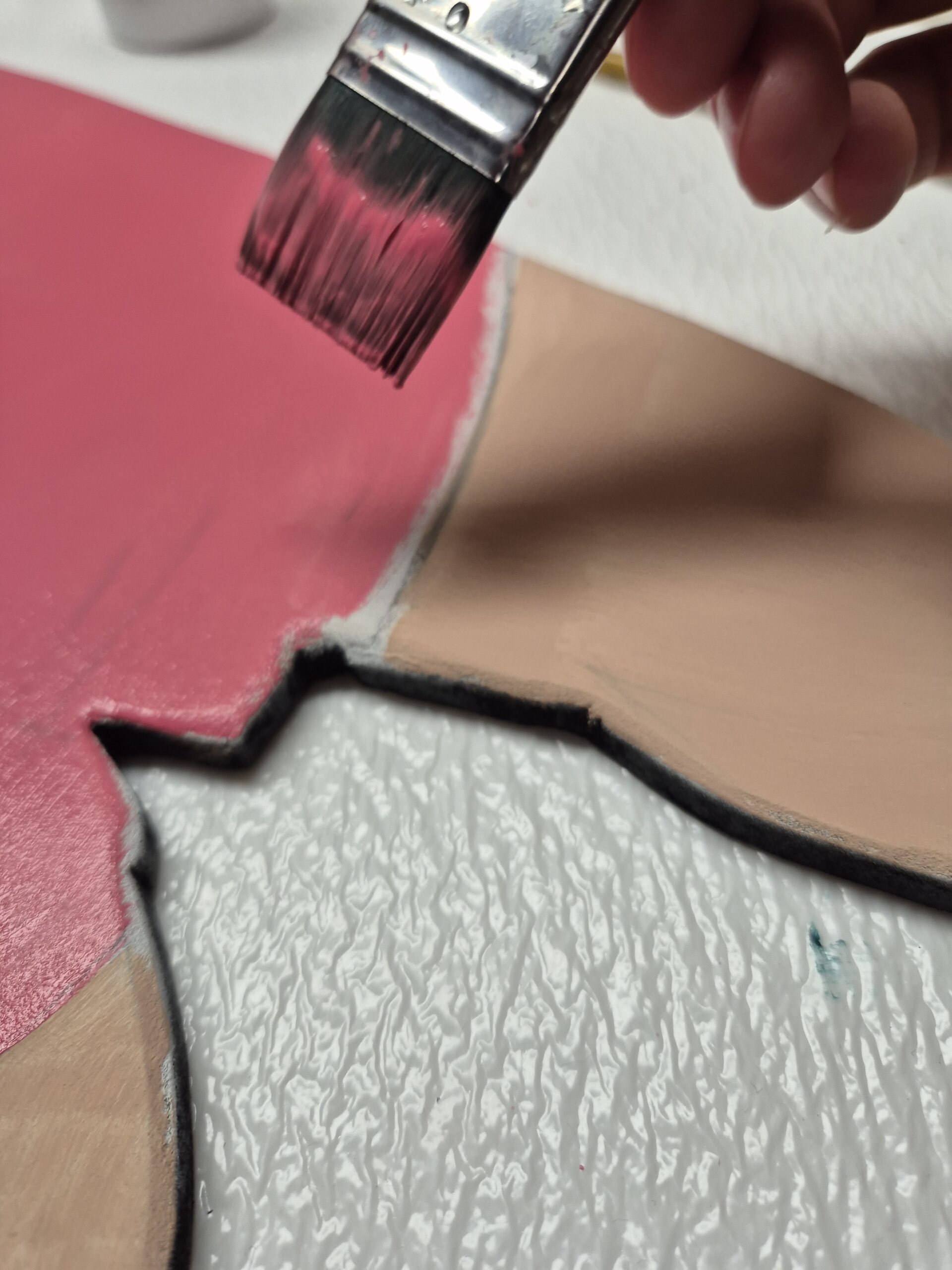 Ein Pinsel streicht rosa Farbe auf eine Holzfläche
