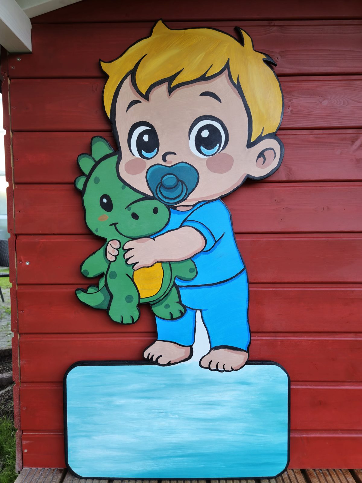 Baby-Junge mit Schnuller und grünem Drachen auf bemalter Holztafel