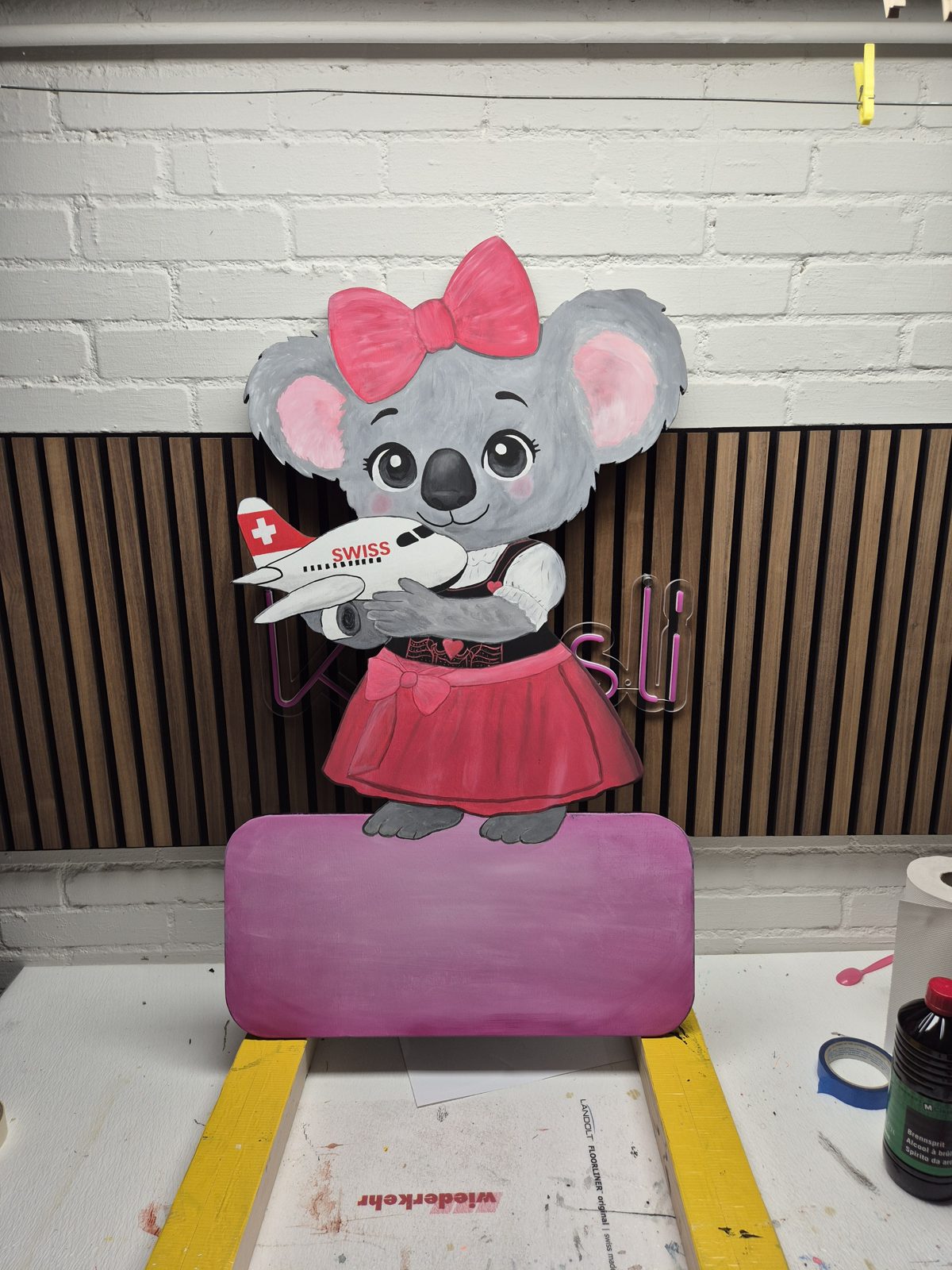 Koala mit rosa Schleife und Flugzeug in der Hand