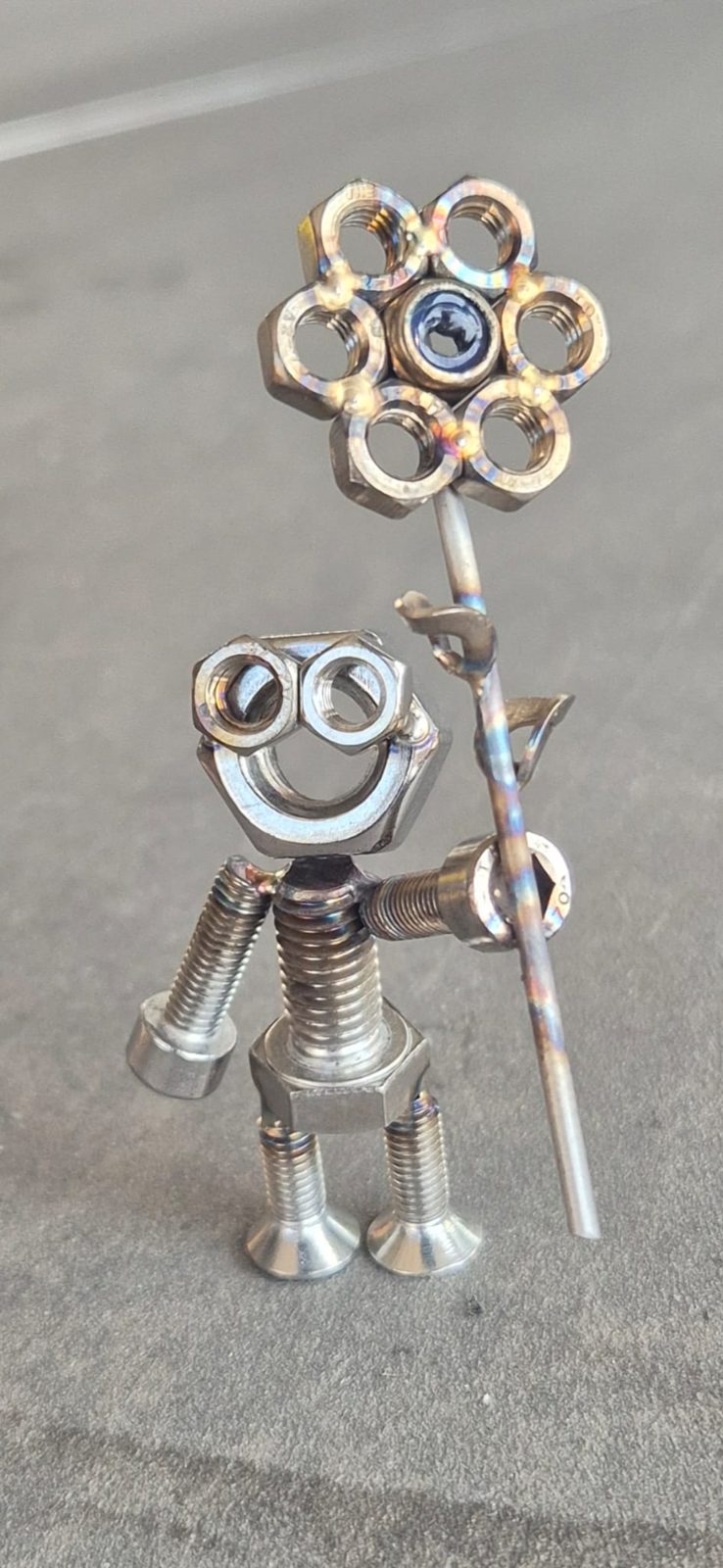 Metallmännchen aus Schrauben und Muttern hält eine Blume aus Muttern