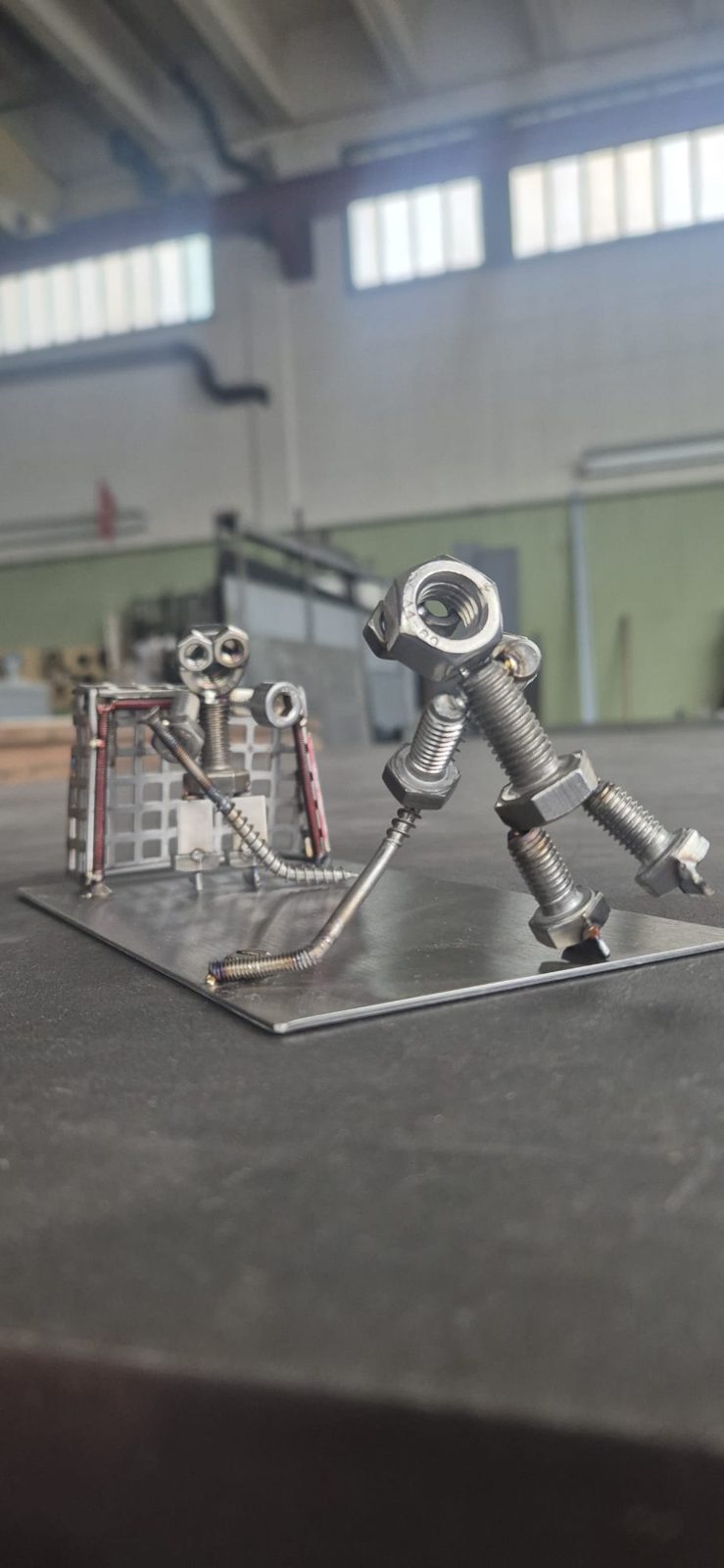 Metallmännchen mit Stock neben einem Gittertor