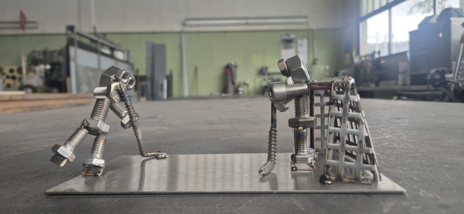 Zwei Metallmännchen beim Spiel vor einem Gittertor