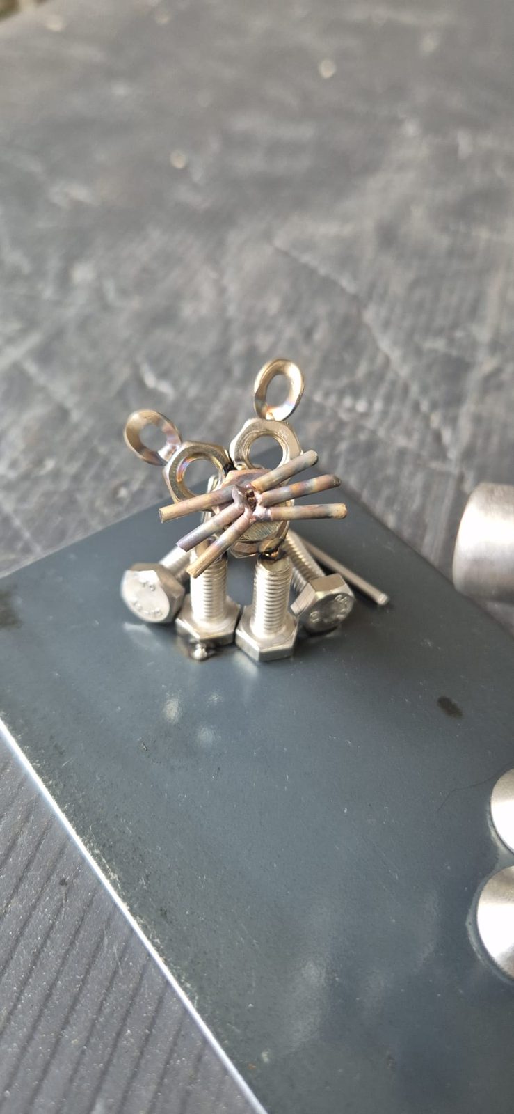 Kleines Metalltier aus Muttern und Draht auf einer Stahlplatte