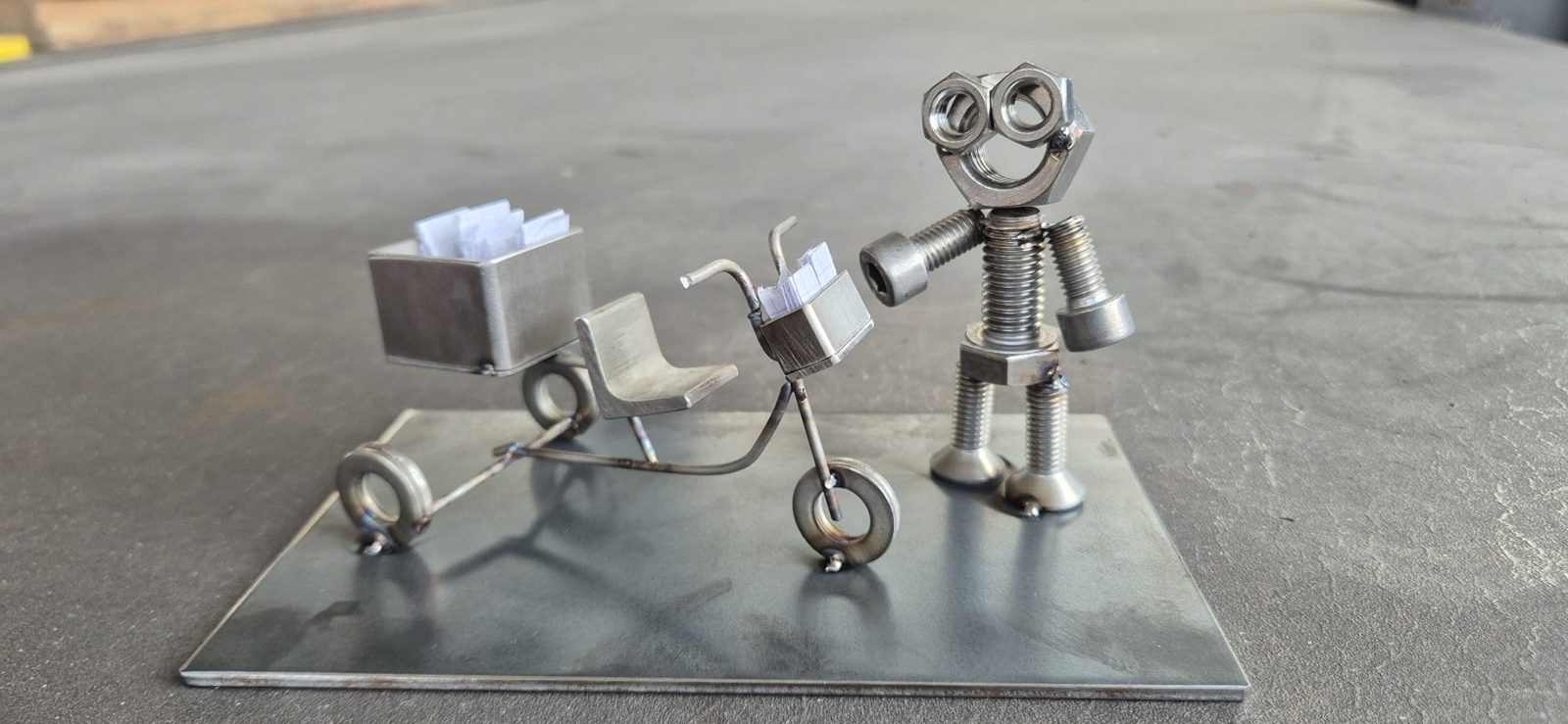 Metallmännchen mit Karre und Dreirad auf einer Stahlplatte